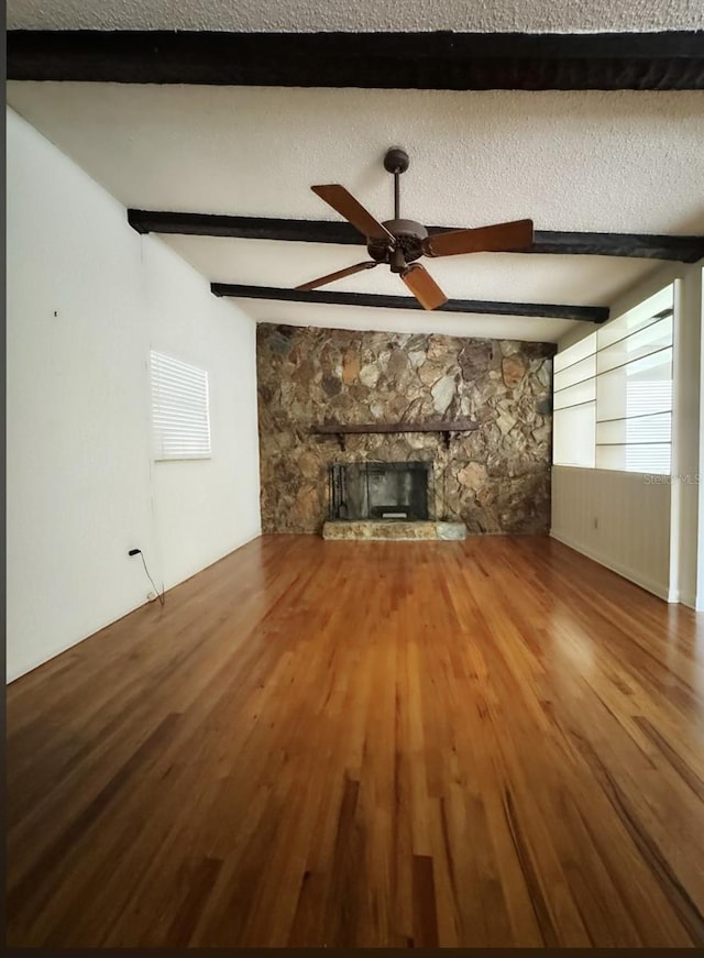 unfurnished living room featuring beam ceiling, a stone fireplace, ceiling fan, and a textured ceiling