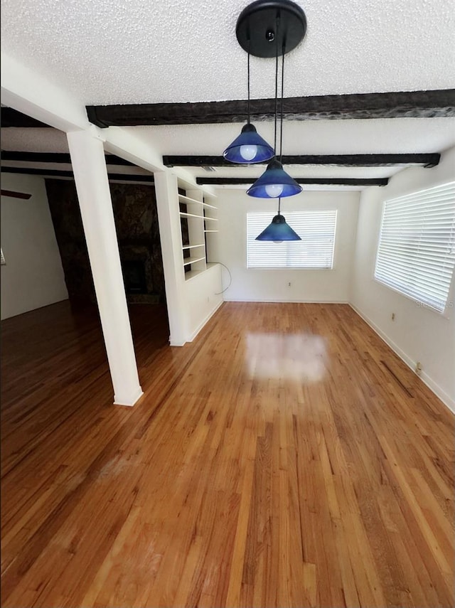 unfurnished living room with beamed ceiling, built in features, a textured ceiling, and hardwood / wood-style flooring