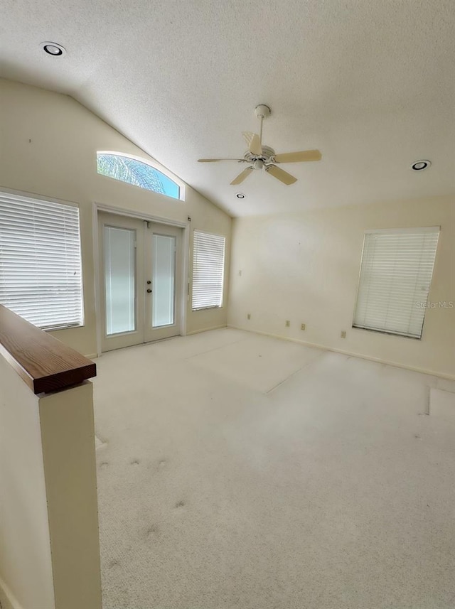 carpeted empty room with ceiling fan, vaulted ceiling, a textured ceiling, and french doors