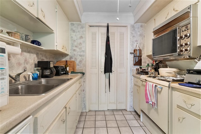 kitchen with ornamental molding, white range oven, sink, light tile patterned floors, and white cabinetry