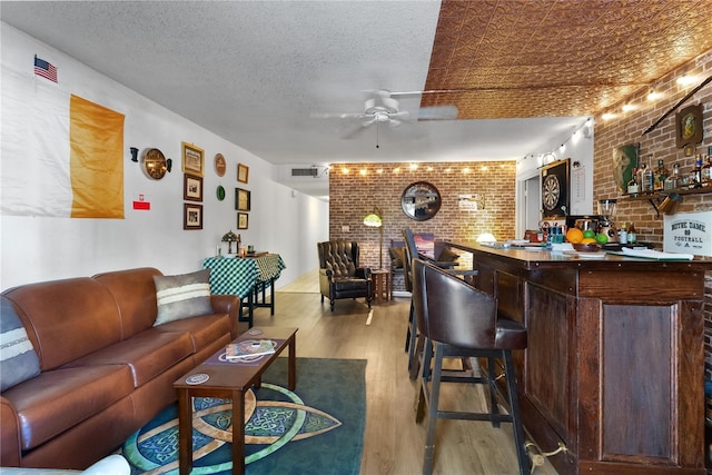 bar featuring dark brown cabinetry, ceiling fan, light hardwood / wood-style flooring, brick wall, and a textured ceiling