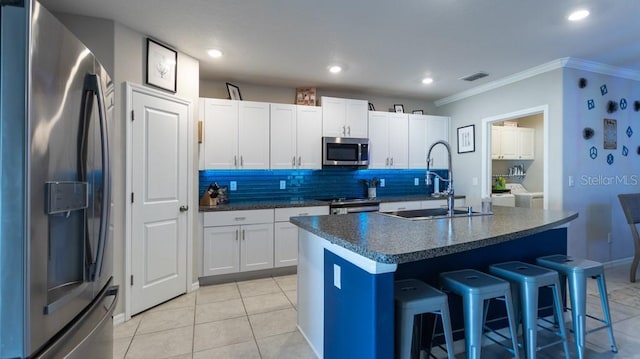 kitchen featuring a kitchen island with sink, sink, appliances with stainless steel finishes, white cabinetry, and a breakfast bar area