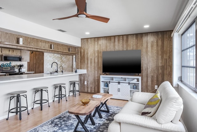 living room featuring wooden walls, sink, and light hardwood / wood-style flooring