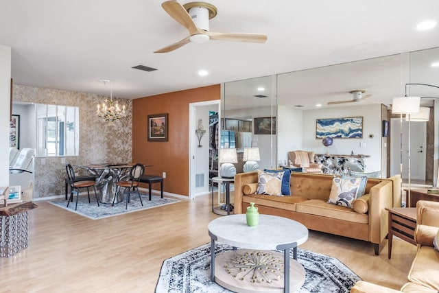 living room with ceiling fan with notable chandelier and light hardwood / wood-style flooring