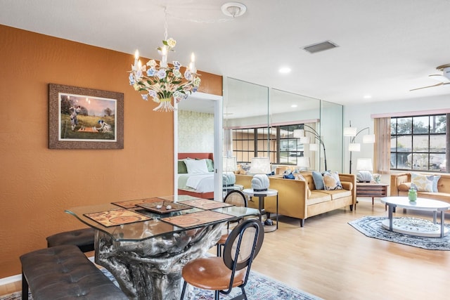 dining space with ceiling fan with notable chandelier and light wood-type flooring