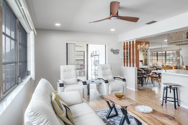 living room featuring ceiling fan with notable chandelier and light wood-type flooring