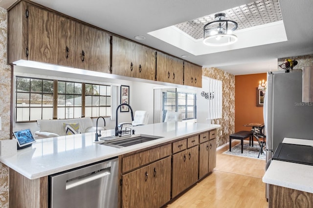 kitchen featuring sink, stainless steel appliances, an inviting chandelier, a tray ceiling, and light wood-type flooring