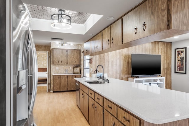 kitchen with appliances with stainless steel finishes, light wood-type flooring, sink, decorative light fixtures, and a chandelier