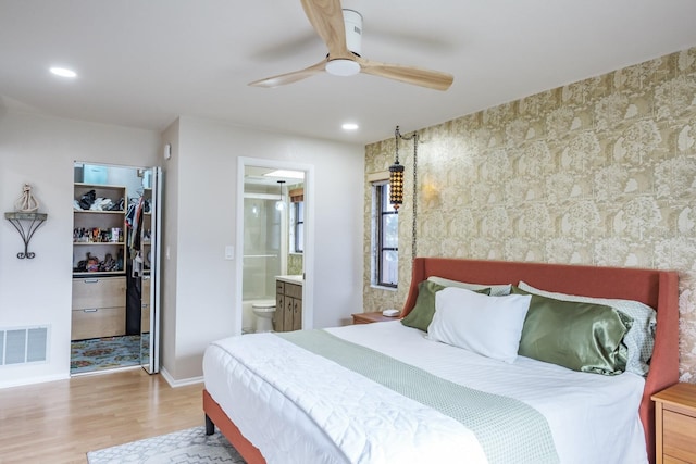 bedroom featuring a walk in closet, light wood-type flooring, ensuite bath, ceiling fan, and a closet