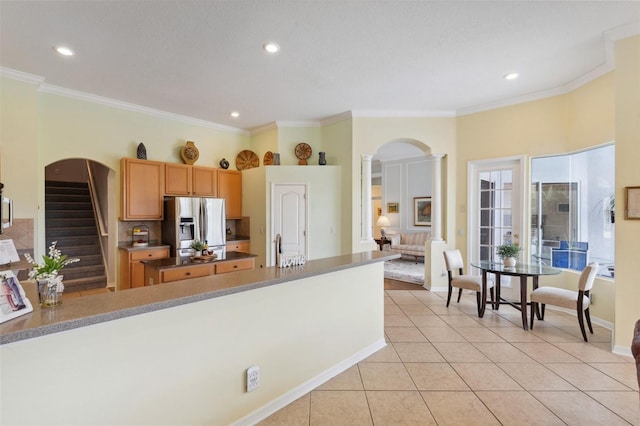 kitchen featuring ornate columns, stainless steel refrigerator with ice dispenser, light tile patterned floors, and ornamental molding