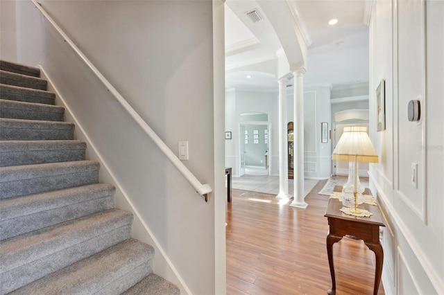 stairway featuring hardwood / wood-style floors, ornate columns, and crown molding