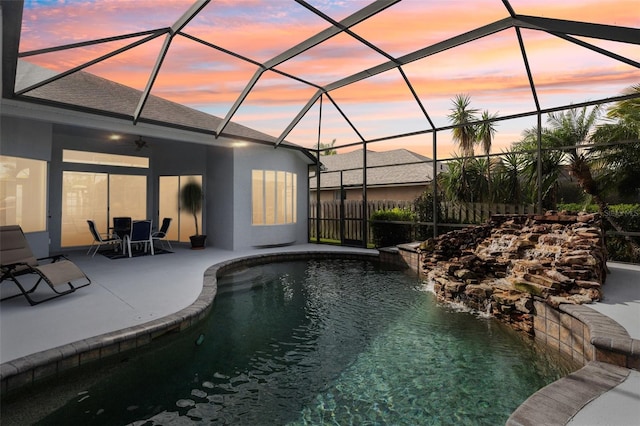 pool at dusk with pool water feature, ceiling fan, a lanai, and a patio