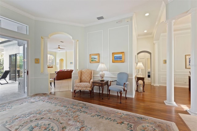 living area with light hardwood / wood-style flooring, ceiling fan, ornamental molding, and ornate columns