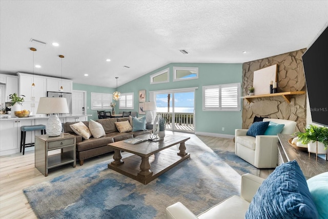 living room with vaulted ceiling, a textured ceiling, a fireplace, and light hardwood / wood-style floors