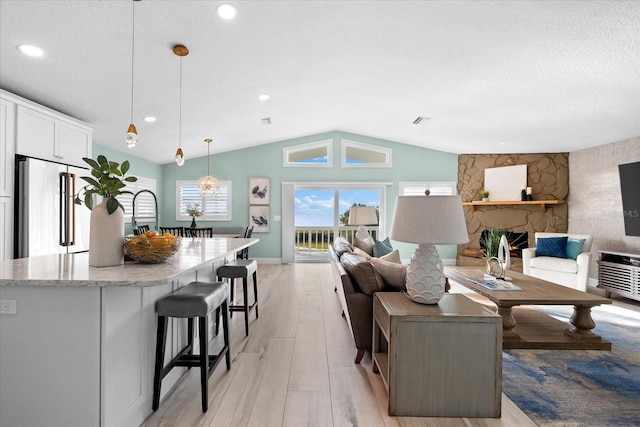 living room featuring lofted ceiling, a fireplace, a textured ceiling, and light wood-type flooring