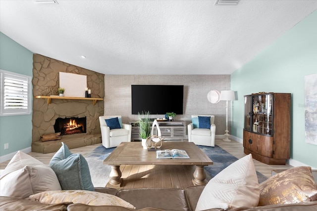 living room with vaulted ceiling, a stone fireplace, wood-type flooring, and a textured ceiling