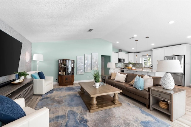 living room featuring lofted ceiling, sink, and a textured ceiling