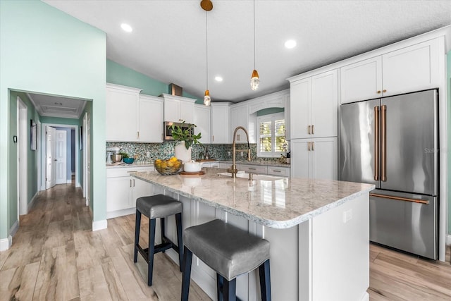 kitchen with high quality fridge, lofted ceiling, white cabinets, hanging light fixtures, and a center island with sink