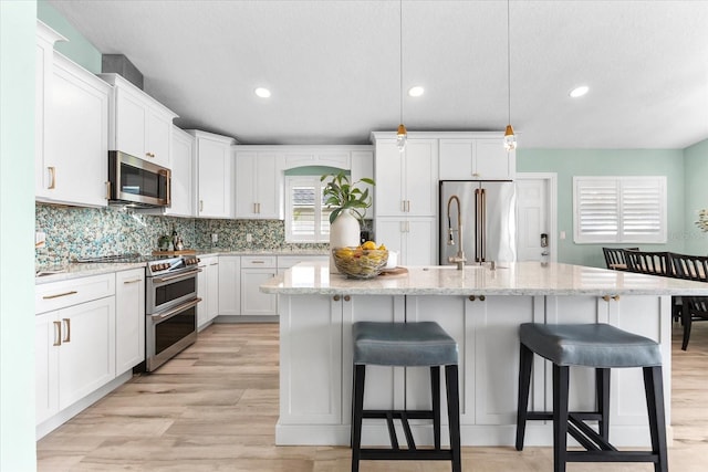 kitchen featuring appliances with stainless steel finishes, decorative light fixtures, white cabinetry, an island with sink, and decorative backsplash