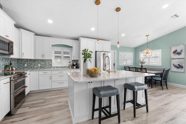 kitchen featuring appliances with stainless steel finishes, a kitchen island with sink, hanging light fixtures, and white cabinets