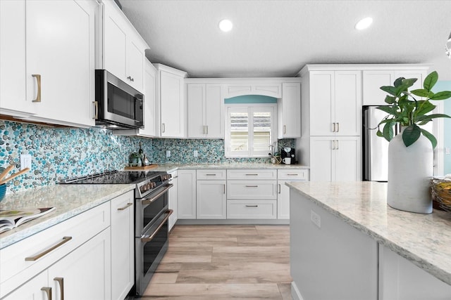 kitchen with backsplash, light stone countertops, white cabinets, and appliances with stainless steel finishes