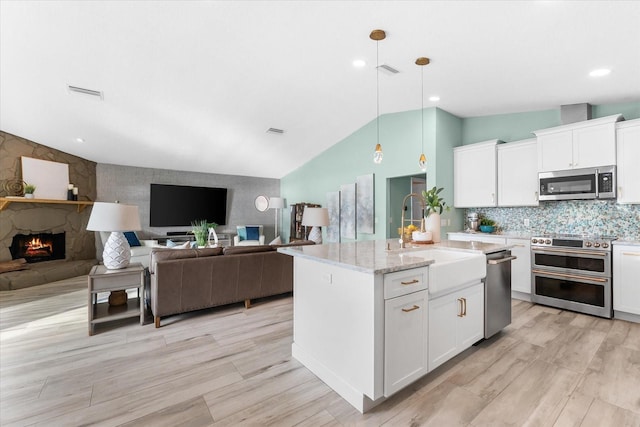 kitchen with white cabinetry, hanging light fixtures, a center island with sink, stainless steel appliances, and a fireplace