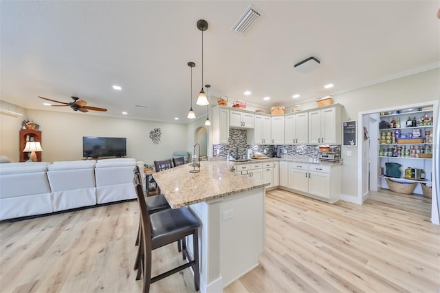 kitchen featuring light stone countertops, a kitchen breakfast bar, kitchen peninsula, pendant lighting, and white cabinets