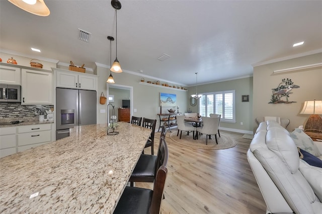 kitchen with a kitchen breakfast bar, white cabinetry, ornamental molding, and appliances with stainless steel finishes