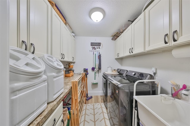 washroom featuring cabinets, sink, independent washer and dryer, a textured ceiling, and light hardwood / wood-style floors