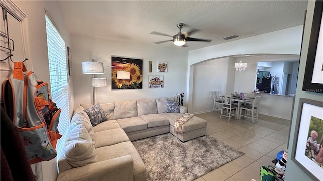 living area featuring arched walkways, visible vents, light tile patterned flooring, ceiling fan, and a textured ceiling