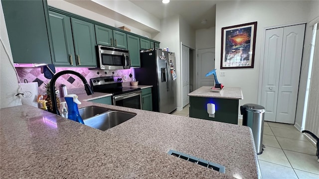 kitchen featuring light tile patterned floors, backsplash, green cabinets, appliances with stainless steel finishes, and a sink