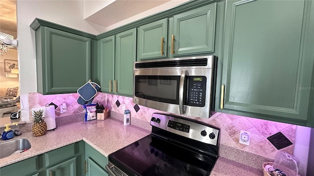 kitchen featuring light countertops, backsplash, appliances with stainless steel finishes, a sink, and green cabinetry