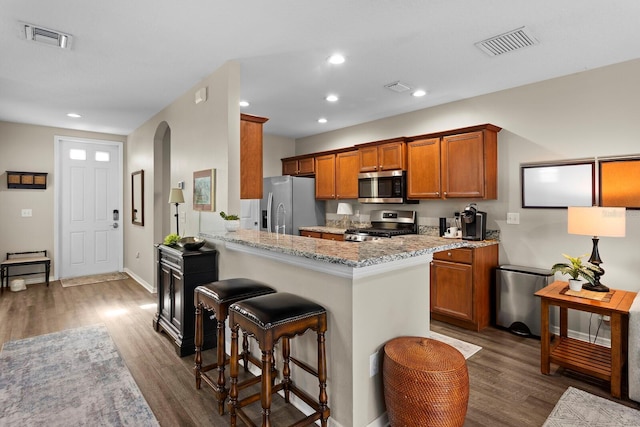 kitchen with stainless steel appliances, light stone counters, dark hardwood / wood-style floors, kitchen peninsula, and a breakfast bar