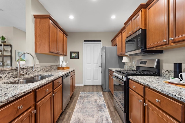 kitchen with appliances with stainless steel finishes, dark hardwood / wood-style flooring, light stone counters, and sink