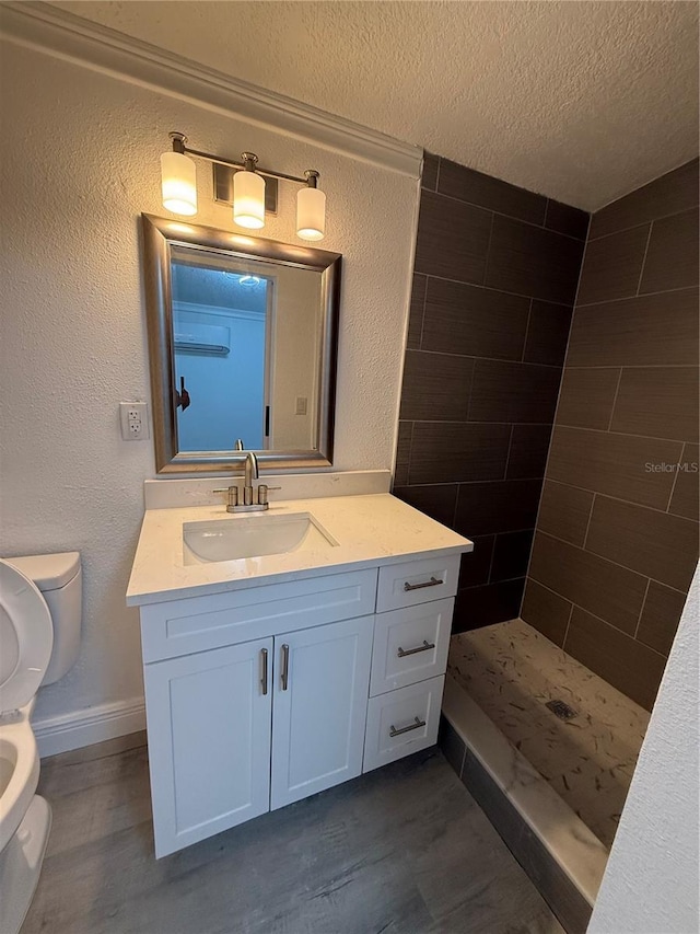 bathroom featuring toilet, wood-type flooring, a textured ceiling, a tile shower, and vanity