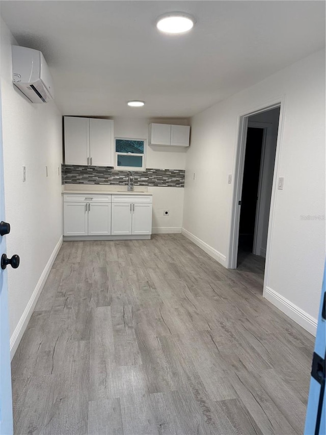 kitchen featuring white cabinets, light wood-type flooring, decorative backsplash, and an AC wall unit