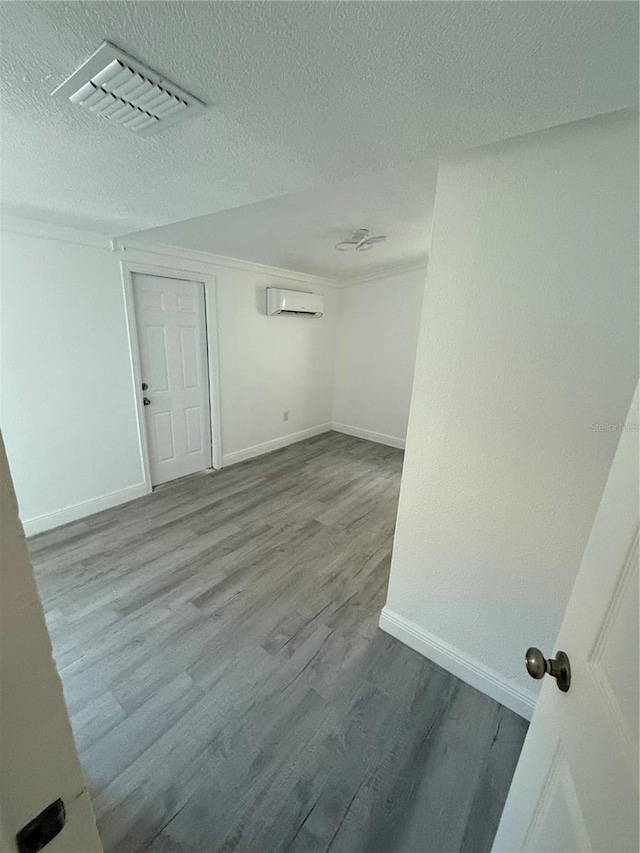 empty room featuring an AC wall unit, a textured ceiling, and light wood-type flooring