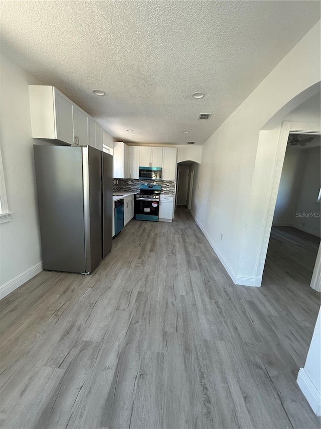 kitchen featuring decorative backsplash, appliances with stainless steel finishes, white cabinets, and light hardwood / wood-style flooring