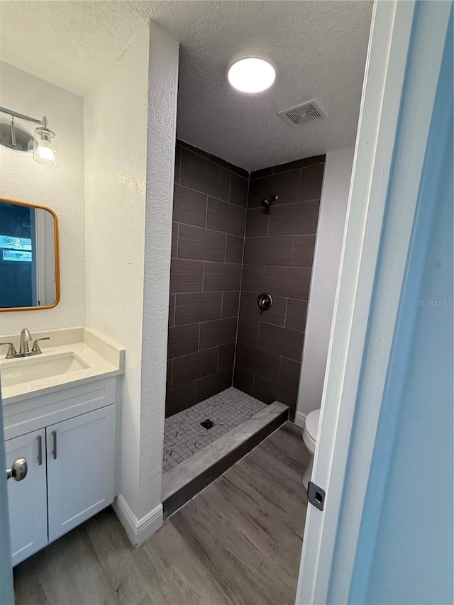 bathroom featuring a tile shower, hardwood / wood-style floors, vanity, toilet, and a textured ceiling