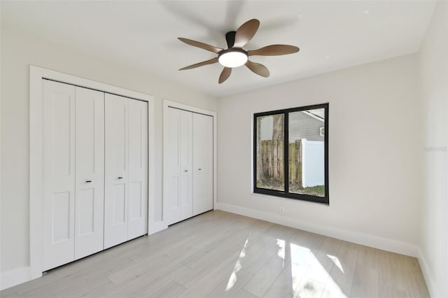 unfurnished bedroom with ceiling fan, light hardwood / wood-style flooring, and multiple closets