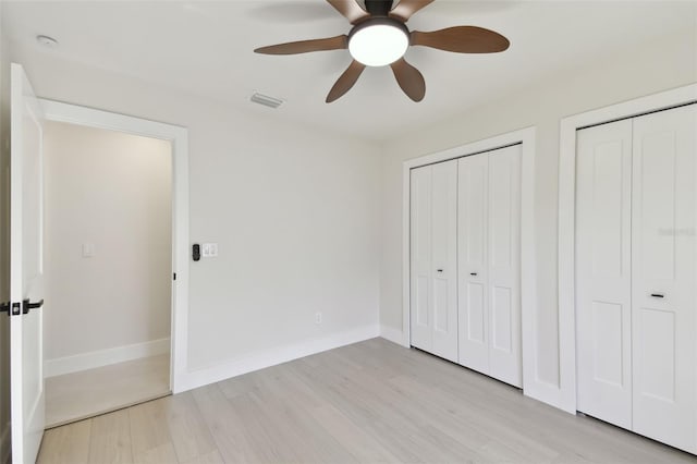 unfurnished bedroom featuring ceiling fan, light hardwood / wood-style floors, and two closets