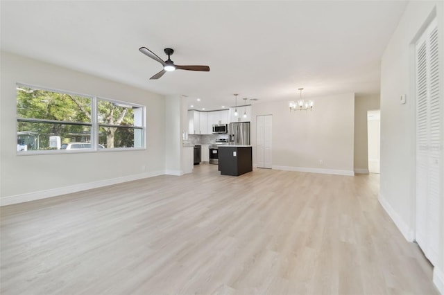 unfurnished living room featuring ceiling fan with notable chandelier and light hardwood / wood-style flooring