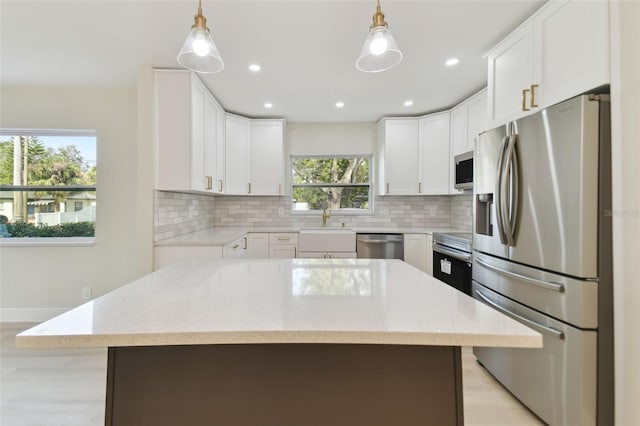 kitchen with white cabinets, a kitchen island, stainless steel appliances, and hanging light fixtures