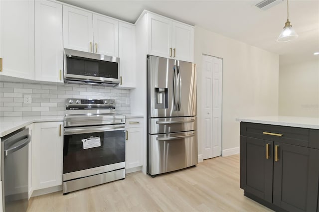 kitchen with pendant lighting, light wood-type flooring, tasteful backsplash, white cabinetry, and stainless steel appliances