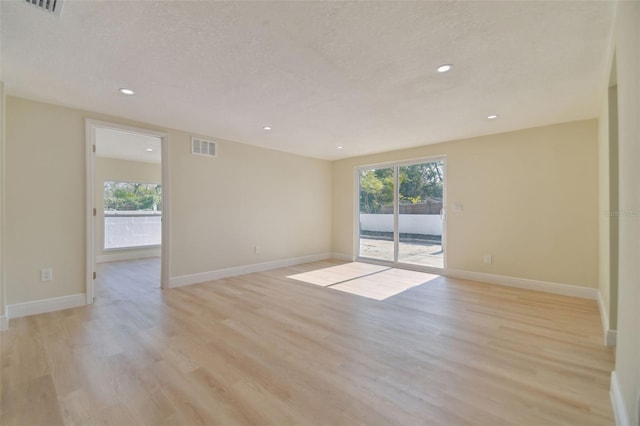 empty room featuring a wealth of natural light, a textured ceiling, and light wood-type flooring