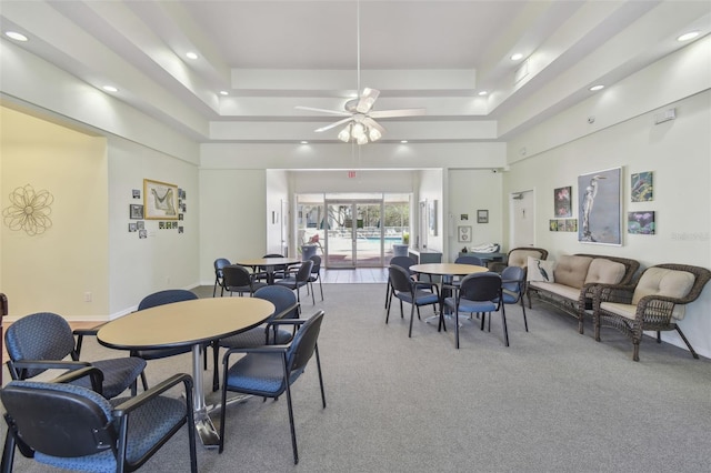 carpeted dining space with ceiling fan, a raised ceiling, and a towering ceiling