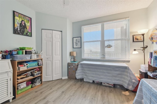 bedroom with a textured ceiling, a closet, light wood-type flooring, and multiple windows