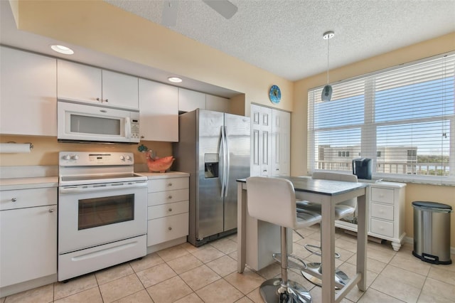 kitchen with decorative light fixtures, light tile patterned floors, white appliances, a textured ceiling, and white cabinets