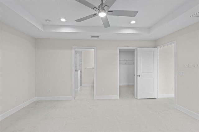 unfurnished bedroom with a raised ceiling, a spacious closet, a closet, and ceiling fan