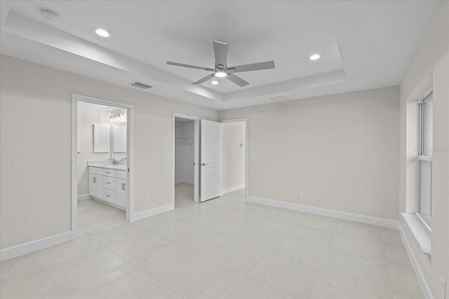 unfurnished bedroom with a walk in closet, ensuite bath, a raised ceiling, ceiling fan, and a closet